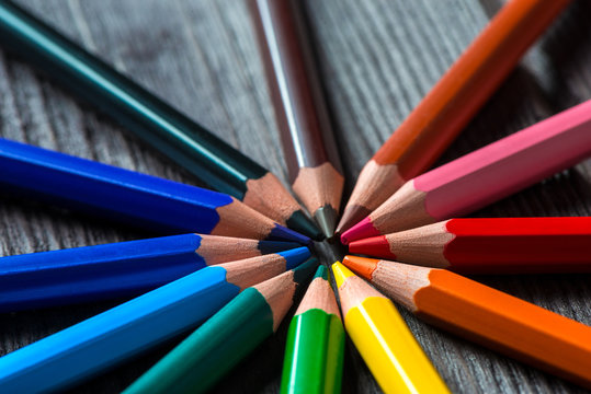 bright color pencils lie on a wooden table forming a circle, closeup photo