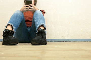 Young girl with a smart phone in her hands sitting on the wooden floor. ,sending a message