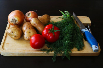 Fresh potatoes and whole onions on wooden cutting board for cooking. 