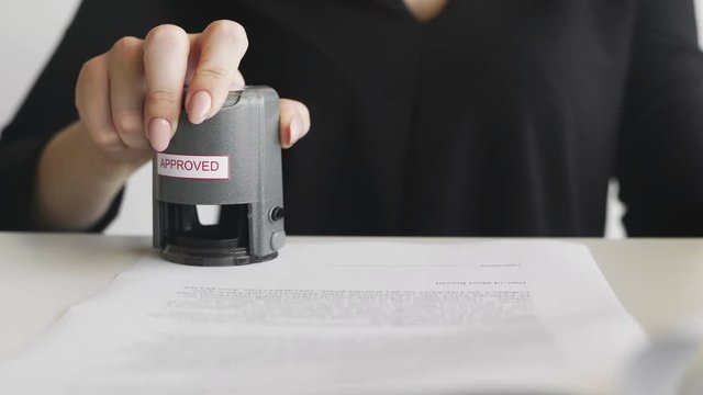 Close up of Female hand that puts an APPROVED stamp in the contract or documents.