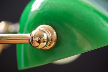 Close-up view of an iconic styled, bankers glass desk lamp. Showing part of the green glass, brass lamp holder, seen on an out of view desk.