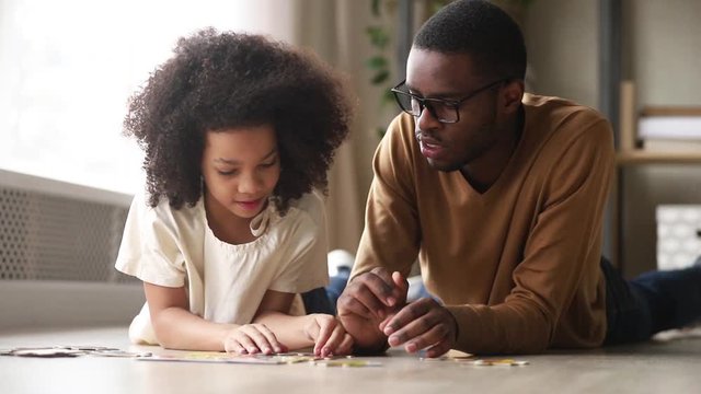 Black father and daughter collect jigsaw puzzle lying on floor
