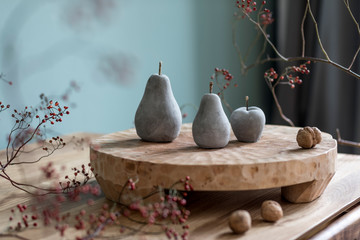 Stylish autumn composition of home decor on living room with wooden fruit tray, cement fruits, nuts and autumn flwoers. Eucalyptus color concpet. Template. Modern decoration. Close up. 