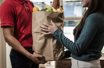smart food delivery service man in red uniform handing fresh food to recipient and young woman...