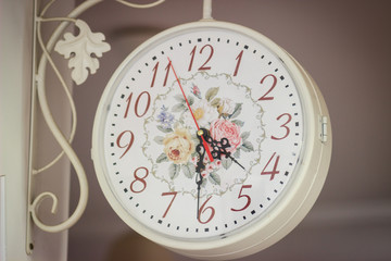 White circle antique clock with flower pattern on the wall in home. It is half past four o'clock.