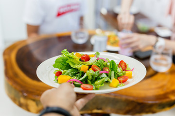 Waiter serving fresh vegetable salad in restaurant.