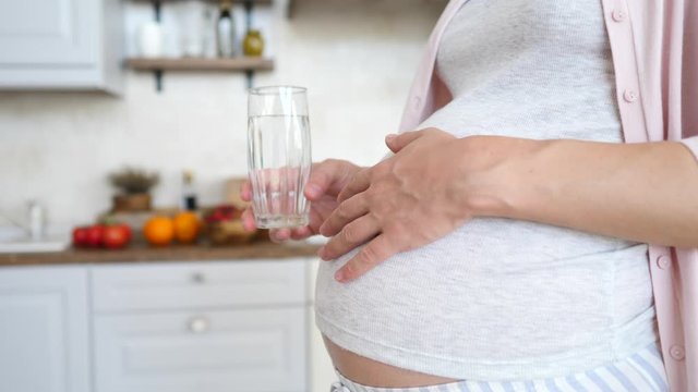 Hydration And Pregnancy Concept. Pregnant Woman Holding Glass Of Water In Kitchen.