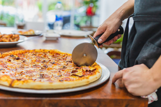 Closeup hand of chef cutting pizza on table.