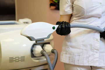 a medical worker in black gloves and a white coat stands next to medical equipment for cosmetology