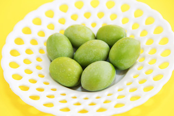 green natural fresh olives in a white decorative plate on a yellow background