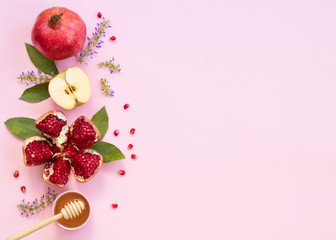 Concept Rosh Hashanah postcard with copy space ; apples, pomegranates and honey on pink background