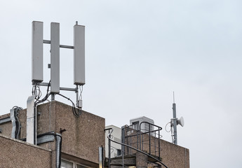 Detailed view of mobile 3G and 4G communications masts and equipment seen on top of a tall office block together with a small microwave dish.