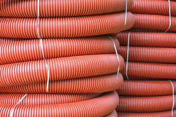 Coils of new red plastic pipe with rain drops. Red plastic tubing for underground cable protection. First floor of a skein of red corrugated tube. Plastic pipes background. Detail of red tube coil