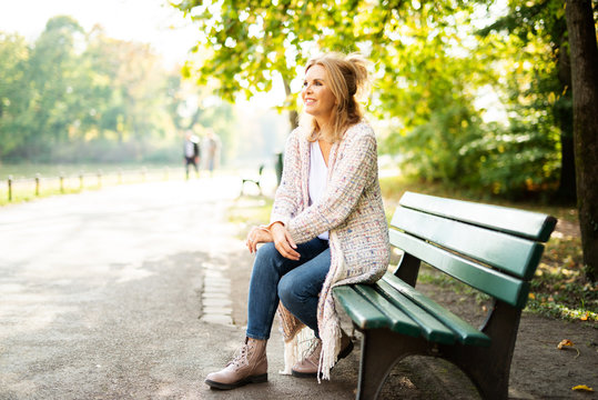 Attraktive Frau im mittleren Alter sitzt im Park auf einer Bank
