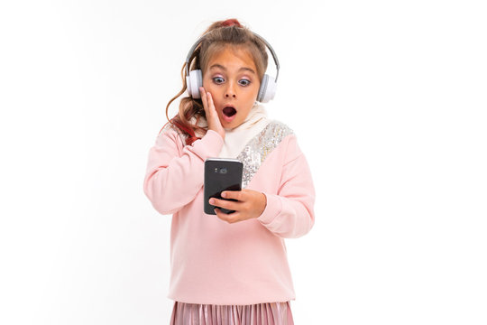 Little happy girl with headphones chatting with friends and is shocked