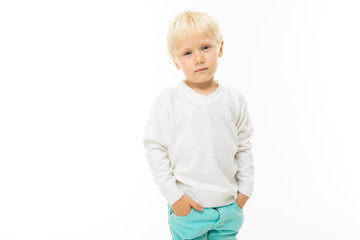 Little boy with short blonde hair, blue eyes, cute appearance, in white jacket, light blue pants, standing with his hands in his pockets