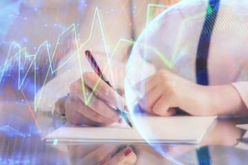 Double exposure of hands making notes with forex chart huds. Stock market concept.