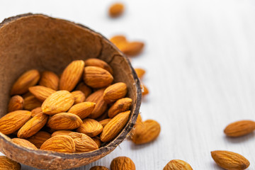 Almond nuts in half coconut shell on white wooden background, side view from above