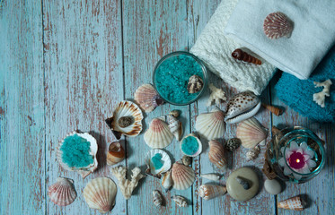 Spa treatment with sea salt.  Colored crystals of sea salt, towels, burning floating candles, shells and corals on a light blue wooden background.