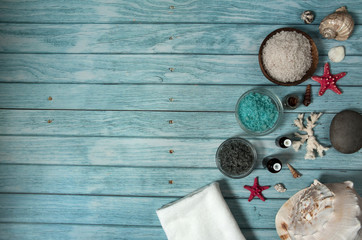 Fototapeta na wymiar Spa treatment with essential oils and sea salt. The border is made of colored sea salt, small bottles of essential oils, starfish, shells and corals on a light blue wooden background.