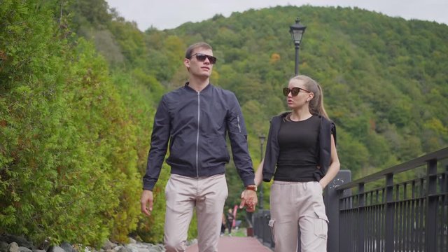 A guy and a girl are walking in the park. A guy and a girl are walking around Rosa Khutor. Rosa Khutor, Sochi, a young woman and a guy are walking along the street of a ski resort  guy and a girl are 