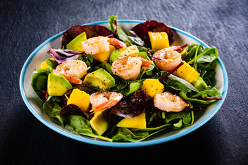 Salad with shrimps on black stone plate