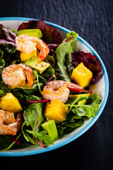Salad with shrimps on black stone plate