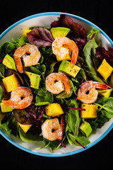 Salad with shrimps on black stone plate