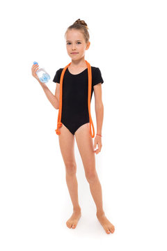 Picture of girl gymnast in black trico in full height with a jumping-rope around her neck and a bottle of water in hand isolated on a white background