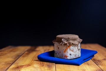 Sauerkraut in the canning jar on the wood table with dark background. Decorated with blue napkin....