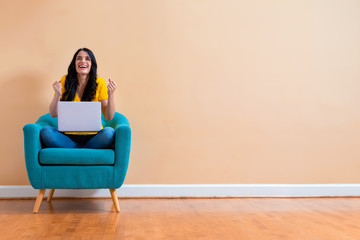 Young woman with a laptop computer with successful pose sitting in a chair