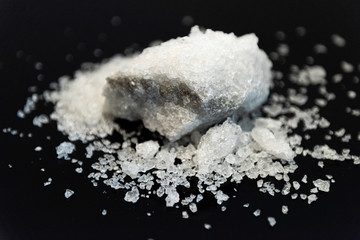 Large crystal of salt on black reflective surface; selective focus; natural edible salt