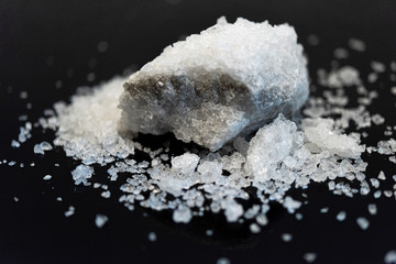 Large crystal of salt on black reflective surface; selective focus; natural edible salt
