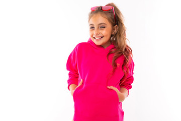 fashionable girl in pink sweatshirt, pink sunglasses is happy and holds her hands in pockets, isolated on white background