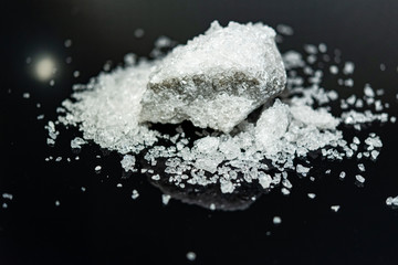 Large crystal of salt on black reflective surface; selective focus; natural edible salt