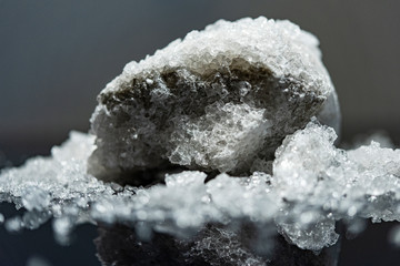 Large crystal of salt on black reflective surface; selective focus; natural edible salt - obrazy, fototapety, plakaty