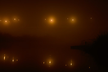 Lights on the bridge over the river in heavy fog. Black and orange long exposure night panorama