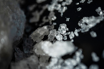 Large crystal of salt on black reflective surface; selective focus; natural edible salt