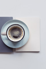 A cup of black coffee stands on a beige and gray book. Top view of the workplace.