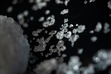Large crystal of salt on black reflective surface; selective focus; natural edible salt