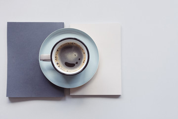 A cup of black coffee stands on a beige and gray book. Top view of the workplace.