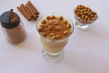 Boza in glass and lebelebi on it and cinnamon next to leblebi in bowl.