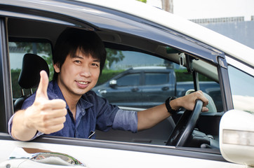Close up of young man smiling and sitting in the modern car with showing thumbs up in his car, For car rent or car business concept.