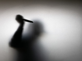 Halloween concept. Blurred shadow of hand holding sharp knife behind white mirror background....