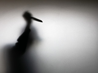 Halloween concept. Blurred shadow of hand holding sharp knife behind white mirror background. Murder scene.