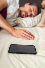 Phone in bed next to a handsome young man that is taking a nap