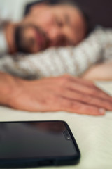 Phone in bed next to a handsome young man that is taking a nap