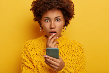 Shocked speechless young Afro woman found photo on social webpage, gasps from wonder, holds modern...