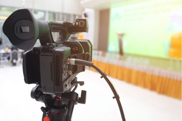Camera filming on a tripod is broadcasting live on stage. Video camera with blurred of the stage background.