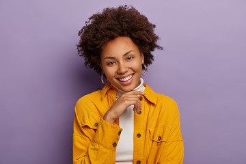 Headshot of lovely happy adult feale smiles pleasantly, shows white teeth, keeps hand under chin,...